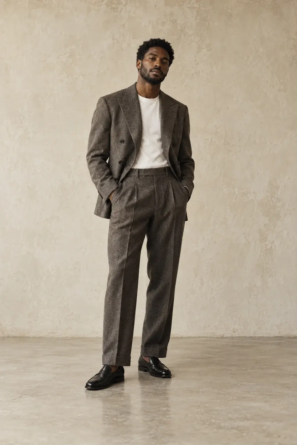 Man in a stone double-breasted blazer and charcoal pleated trousers, hands in pockets